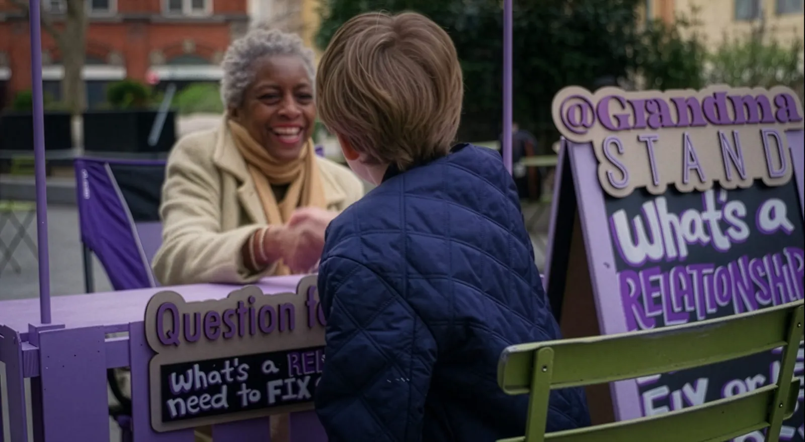 A boy shakes hands with Grandma Jennifer at the Grandma Stand