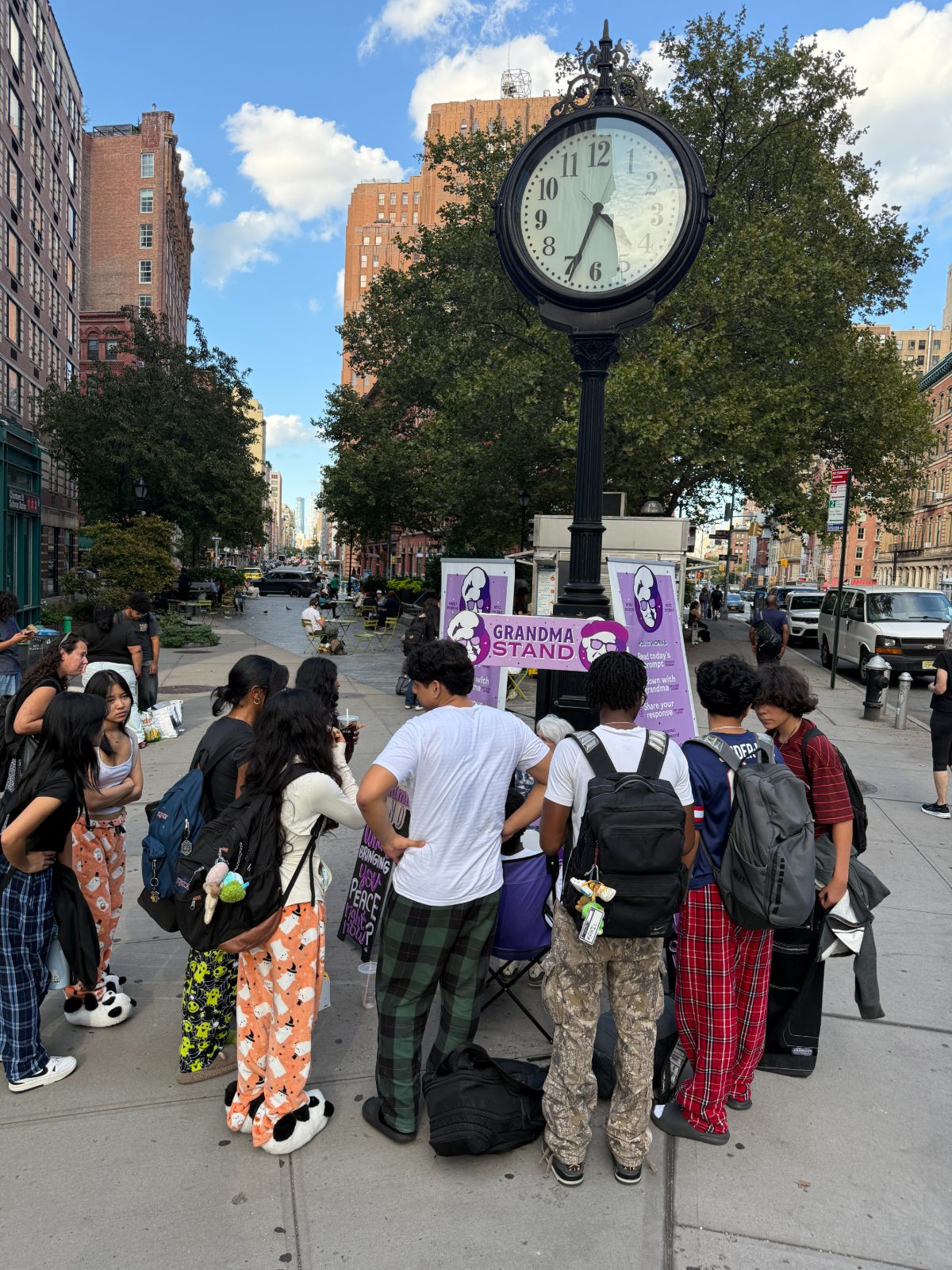 A crowd of teenagers gathered around the stand under a street clock